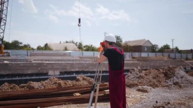Optik Enstrüman kullanan profesyonel inşaat işçisinin arka planda çekimi. Sert şapka ve önlük giyen adam bina planlarının açılarını ölçüyor