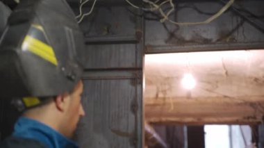 Güvenlik giysisi ve koruyucu maskeli profesyonel kaynakçının yakın çekimi inşaat alanının duvarına metal kaynak yapmaya başlar. Genç işçi çalışma sürecine hazırlanıyor.