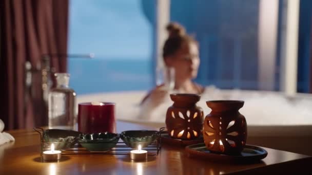 瞑想シーン バスルームの粘土瓶にアロマランプキャンドル 女性は温かい泡風呂でカクテルを飲む 高齢の女性はバスタブの泡に横たわるシャンパンを楽しんでいます ロマンチックな雰囲気 — ストック動画