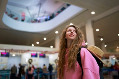 Hasır şapkalı neşeli gezgin havaalanı Noel atmosferinin tadını çıkarıyor. Canlı pembe ceketiyle yeni yıl kaçamağına hazır. Tatil sezonu başlıyor..