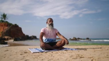 Yaşlı adam, okyanus kıyısındaki cennet adası sahilinde meditasyon yapıyor ve lotusta oturuyor. Zenci erkek kıdemli erkek yoga yaparken bacak bacak bacak üstüne atmış..