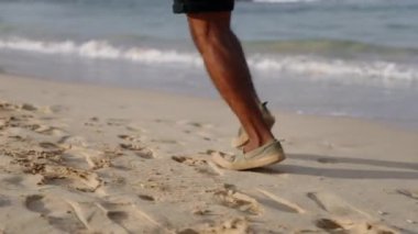 Plajda, mavi okyanus suyu ve tropik adalarda dalgaları olan aktif siyahi kıdemli bir adamın bacakları. Yaşlı gezgin emeklilik koşusu yapıyor, spor yapıyor, sağlıklı ve neşeli bir hayat sürüyor. Yakın çekim..