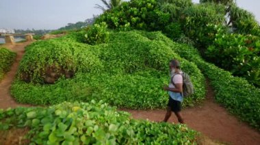 Gri saçlı yaşlı gezgin, tropik ada manzaralı, doğa, okyanus, gökyüzü, egzotik bitkiler ve ormanla tepede tırmanıyor ve tırmanıyor. Yaşlı adam aktif yaşam tarzını, yolculuğunu, maceralarını seviyor..