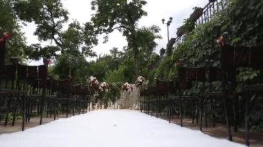 Çiçeklerle süslenmiş açık hava düğün yeri, beyaz koridor koşucusu, düğün için hazırlanan zarif sandalyeler, romantik düğün planlama teması.