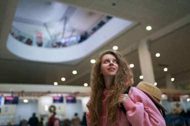 Hasır şapkalı neşeli gezgin havaalanı Noel atmosferinin tadını çıkarıyor. Canlı pembe ceketiyle yeni yıl kaçamağına hazır. Tatil sezonu başlıyor..