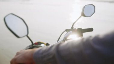 Motosiklet gidonunda motorlu el. Sahilde motosiklet kullanan biri var. Hız göstergesi ve dikiz aynalı bir motosiklet göstergesi. Okyanus kenarında scooter 'da oturan bir adam. Güneş merceği yansımaları parlatır.