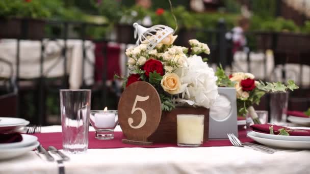 赤と白の色のテーマ 番号付きのセンターピース お祝いのイベントのテーブル設定 花の配置とエレガントな屋外の結婚式のテーブルスケープ ロマンチックな場面 イベントプランナーに最適な映像 — ストック動画