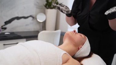 Müşteri güzellik prosedürü sırasında dinleniyor, kuaförde su içiliyor. Profesyonel güzellik uzmanı modern kaplıcalarda cilt bakımı için yüz maskesi takıyor. Cilt bakımı, sağlık rutini..