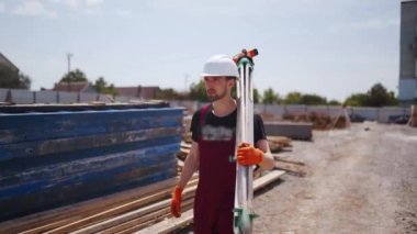 Theodolite Surveying Optical Instrument taşıyan profesyonel inşaat işçisinin görüntüsü. Kasketli ve önlüklü bir adam inşaat alanında yürüyor..
