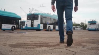 Tramvay parkında yürürken çekilmiş bir fotoğrafı takip ediyorum. Günlük kıyafetli bir sürücü işe başlamak için mavi elektrikli araca gidiyor..