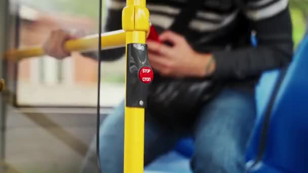 クローズアップショットマンは 移動バスの手すりにある赤い停止ボタンを押すために立ち上がります 男は公共交通機関を降りるために運転者のためのサインを作るために押すボタンを押します — ストック動画