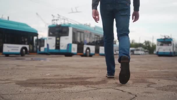 トロリーバスの駐車場を歩いている若者の後ろのショット 仕事の日を始めるために青い電気自動車に向かうカジュアルな服の運転者 — ストック動画