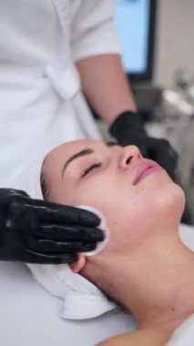 Uzanan kadın için cilt bakımını gençleştirme, cilt bakımına odaklanma, genç görünüm korunması. Eldivenli güzellik uzmanı, kaplıcada yaşlanma önleyici yüz temizleme ameliyatı yapıyor..