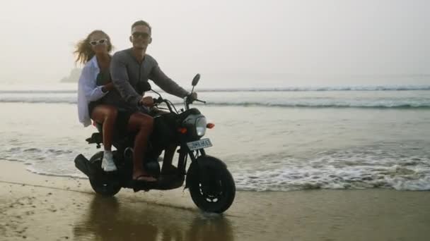 日出时 快乐的人们骑摩托车在海滨泼水 恋爱中的夫妻在海滨驾驶摩托车很开心 女孩拥抱着男朋友 举起手来吹气 太阳耀斑 — 图库视频影像