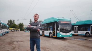 Gündelik giysiler içinde, kolları göğsünde çapraz duran ve tramvayda gülümseyen genç profesyonel erkek sürücü. Arka planda mavi ve beyaz el arabaları var