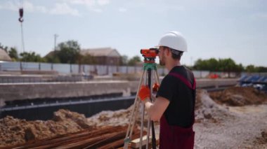 Profesyonel İnşaat İşçisi Teodolit Araştırması Optik Enstrüman Kullanıyor. Sert şapka ve önlük giyen adam bina planlarının açılarını ölçüyor