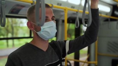 Tıbbi maske takmış, elinde tırabzan taşıyan genç bir yolcunun tramvay yolculuğu görüntülerini yakından çek. Günlük kıyafetler giyen Avrupalı adam toplu taşımacılıkta covid-19 'dan korunuyor.