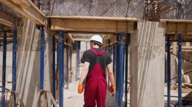 Tablet bilgisayarlı profesyonel inşaat işçisinin arka plandaki görüntüsü. İnşaatçı, yatay biçimlendirmeleri kontrol etmek için inşaat alanındaki monolitik çerçeve yapısı arasında yürüyor.