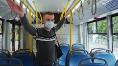 Tıbbi maske takan genç erkek yolcu bir sonraki otobüs durağında trabzandan inmeye hazırlanıyor. Günlük giysili adam toplu taşımacılıkta COVid-19 'dan korunuyor..