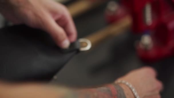 プロのレザー職人が金属の付属品を取付けるためのハンドプレスが付いているハンドバッグにピンに近づきます タトゥーを持つ男は ワークショップで特別なツールで財布を作ります — ストック動画