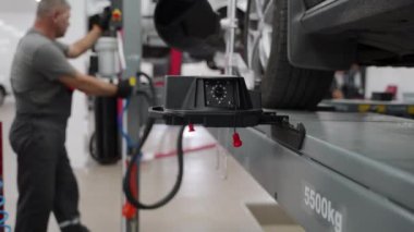 Uzman araç bakımı yapar, güvenlik için uygun hizayı sağlar. Otomobil tamircisi araba tekerleklerini garajda yüksek hassasiyetli ekipmanlarla hizalar. Araç düzgün bir bakım için kaldırıldı..