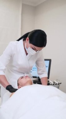 Uzman terapist tarafından cilt bakımı. Maskeli profesyonel güzellik uzmanı kaplıcadaki kadın müşteriye yaşlanma karşıtı yüz masajı yapıyor. Müşteri boyun terapisi sırasında dinlenir, güzellik kliniğinde gençleşir..