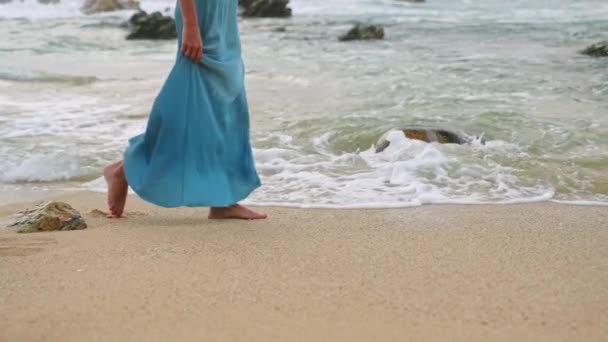 ドレスの女性はビーチに沿って裸足を散歩します 青いガウンのエレガントな女性は 穏やかな波 穏やかなビーチシーン 静かな休日を通って歩きます 夏休み 旅行をリラックス — ストック動画