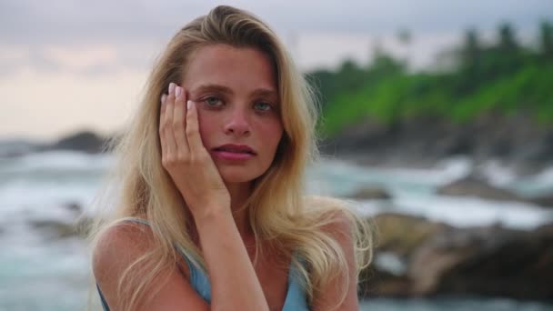 自然妆容的女人 海滨孤寂的柔滑的头发 优雅的女性触摸着脸 站在奇异的海滩上 平静的海浪 暑假护肤产品 宁静型 — 图库视频影像