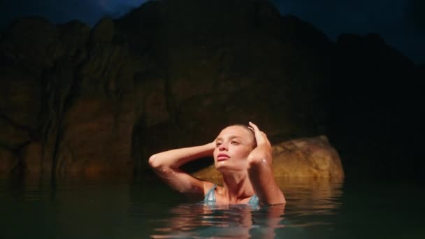 优雅的女士在月光下享受宁静的海水浴 穿着蓝色衣服的天真无邪的美女沉浸在夜海中 身后是岩石 奢华时尚的场面 神秘的海岸氛围 宁静的水温时刻 — 图库视频影像
