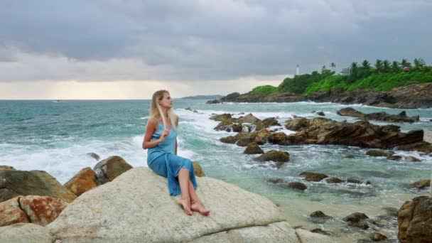宁静的气氛有助于与沮丧作斗争 减轻大自然的压力 女性在岩石沙滩上沉思 在海浪中精神健康 女人坐在悬崖上俯瞰大海 感到宁静 — 图库视频影像