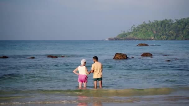 Mirissa Sri Lanka January 2021 老年人在当地的帮助下享受热带海滩 斯里兰卡青年在海上帮助老年妇女 代际护理 旅行包容显示 — 图库视频影像