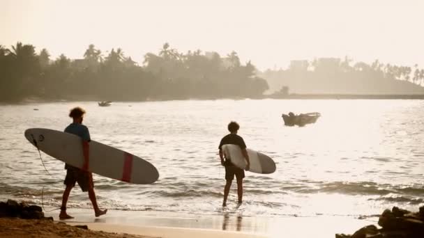 斯里兰卡米莉莎 2021年1月19日 一对带冲浪板的合适男人在日出时进入海水 空船在波浪中颠簸 运动员们在海里冲浪 棕榈树的轮廓 — 图库视频影像