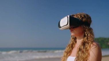 Bağdaş kurmuş, sanal gerçekliği sakin bir yere taşır, modern rahatlama teknolojisi doğayla harmanlanır. Sarışın kadın güneşli sahilde meditasyon için VR kulaklık kullanıyor..