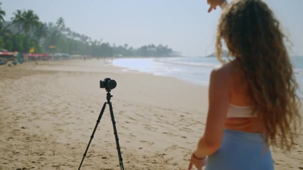 充满活力的海滨环境增强了观众的视觉效果 卷发女子在热带海滩上表演舞蹈 带着相机在三脚架上拍摄内容 分享社交媒体 — 图库视频影像