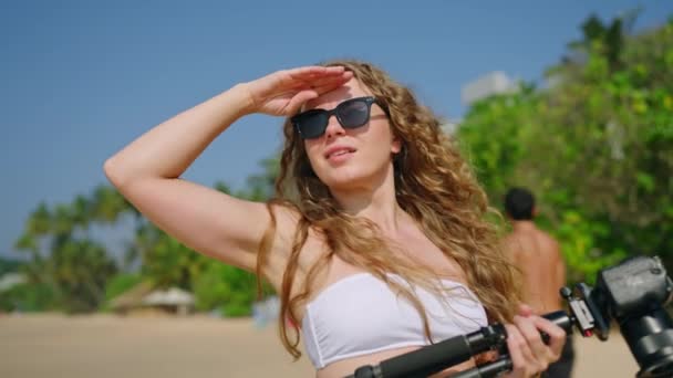 太阳镜装饰的摄影师冲刷热带地区 意图创造内容 熟悉旅行的女人寻求迷人的海滩背景 平衡相机以获得最佳拍摄效果 — 图库视频影像