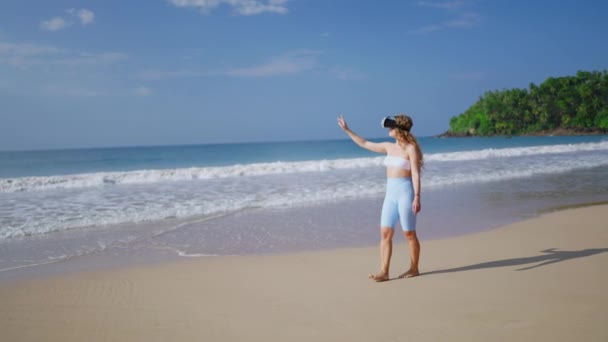 互动技术冒险 触摸手势互动 沉浸在模拟海滨环境中 戴Vr耳机的女人探索海滩上的虚拟热带地区 海浪在附近翻滚 慢动作 — 图库视频影像