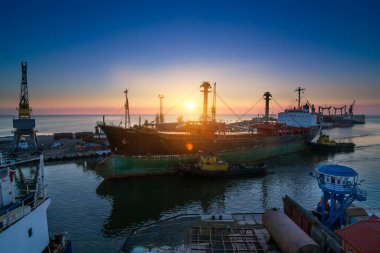 Kargo konteynerleri uluslararası taşıma için hazır. Ticari gemiler limana yanaştı, gündoğumu arka aydınlatma gemileri. Nakliye endüstrisi çalışıyor, şafakta küresel ticaret. İskele altyapısı görünür.