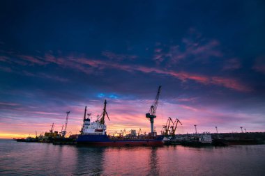 Günbatımı siluet vinçleri, küresel ticarete hazır araçlar. Konteyner gemisi sanayi limanına yanaştı. Deniz taşımacılığı, lojistik. Nakliye, liman tesisleri, denizcilik ihracatı.
