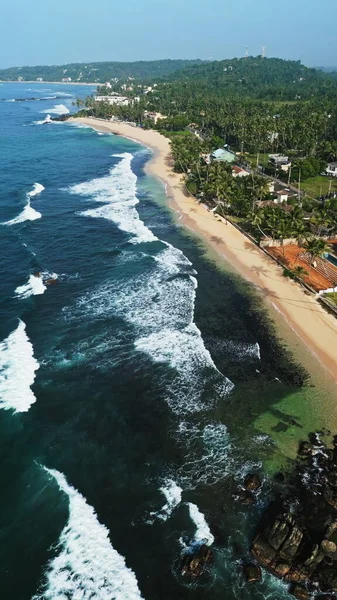 Vacationers enjoy tropical lagoon, swim in clear waters, relax on serene coastline. Aerial view reveals Dalawella beach turquoise waters, swaying palms, golden sands in Sri Lanka.