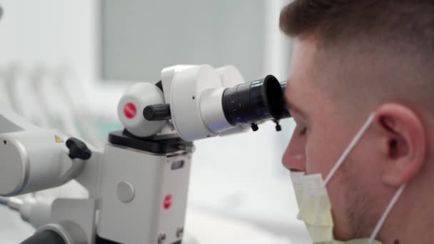 医薬品実験室で顕微鏡を用いた保護フェイスマスクにおける男性科学者の閉鎖 微生物学者はワクチンの実験を行っている 科学者は顕微鏡を用いた研究サンプルを研究する — ストック動画