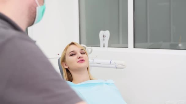 現代歯科クリニックで歯の椅子に横たわっている若い女性 女性患者は歯を白くするのを待っています ブロンドの女性は私立診療所で医療処置のために準備します 歯科医は椅子を調節する — ストック動画