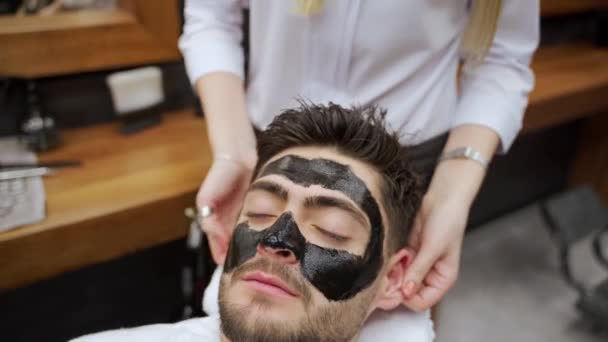 ビーガニックは スキンケア 気孔クレンジングのためにクライアントに炭の顔を適用します 男性は床屋で黒いマスクの治療を受けます プロサロンで培ったメンズグルーミングのためのスパサービス — ストック動画