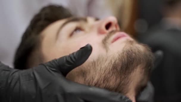接受治疗的男性享受专业的护肤治疗 戴着手套的理发师给商店里的男性顾客提供宽松的脖子和面部按摩 专业按摩师致力于缓解面部紧张 缓解压力 — 图库视频影像