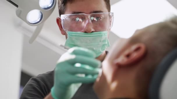 男性歯科医は 現代の歯科クリニックで患者の歯を治療します 歯科医は歯科オフィスで歯を掃除しています 男性クライアントのための歯を充填する医師 根管を治療します クローズアップ — ストック動画