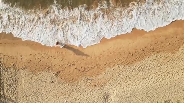 海の波で砂浜を歩くドレスで女性を撮影し ハイアングルショットは海岸沿いの平和で孤独な散歩をハイライトし 自然の中で穏やかなマインドフルな瞬間を作成します — ストック動画