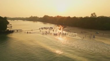 Neşeli çocuklar plaj oyunlarını ve deniz kenarı eğlencesini sever, sahilin karanlık anlarını yakalar. Gün batımında okyanusun kenarında oynayan çeşitli beyaz üniformalı çocukların hava manzarası.