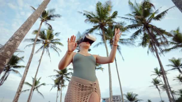 在虚拟世界中激发用户的手势 模拟异化体验 戴Vr耳机的女性探索棕榈树间的数字世界 热带环境下的创新科技化身互动 — 图库视频影像