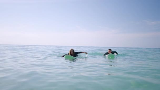 サーフボードで水着のパドリングでサーファー 水着の女性は セッション後に海岸で泳いでいます 恋するカップルは船の上の海水からやってきます 家族旅行のレクリエーション活動 関係ゴール — ストック動画