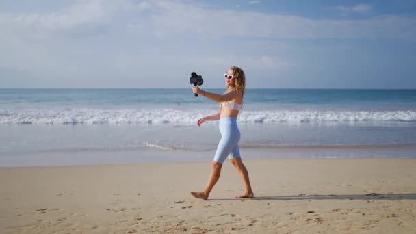 旅游博主捕捉海洋景观 分享冒险经历 分享技巧 身穿白色服装的影响者用专业相机 无线Lav麦克风记录海滩博客 内容创造者吸引了观众 阳光沿海的位置 — 图库视频影像