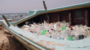 Çöpe atılmış plastik şişeler kumlu sahildeki terk edilmiş tekneleri dolduruyor. Çevresel deniz enkazı sorunu. Dalgalar arkadan çarpar, okyanus kirliliği. Kıyı temizliği için acil durum. Çöp, çöp, çöp yığını..